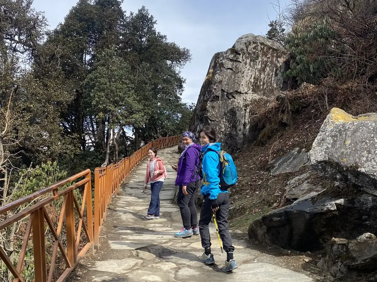 Three trekkers pausing on the stone-paved Tungnath–Chandrashila trail beside a wooden railing