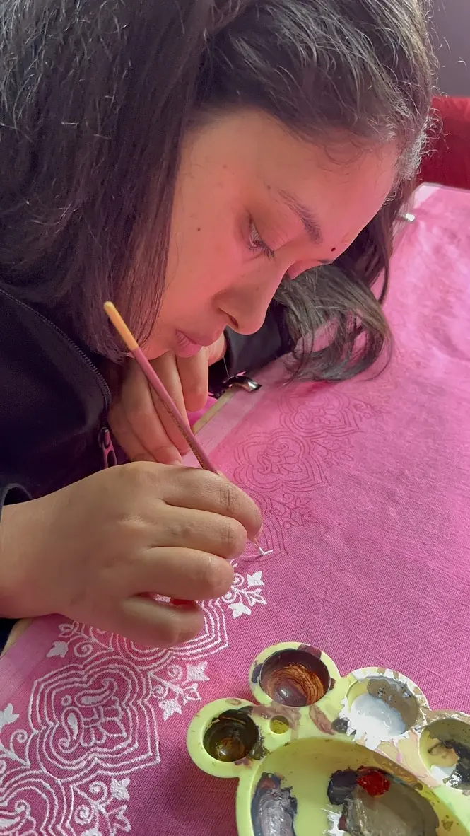 Kajal painting a traditional Aipan motif by hand on pink fabric, with geru and rice-paste pigments