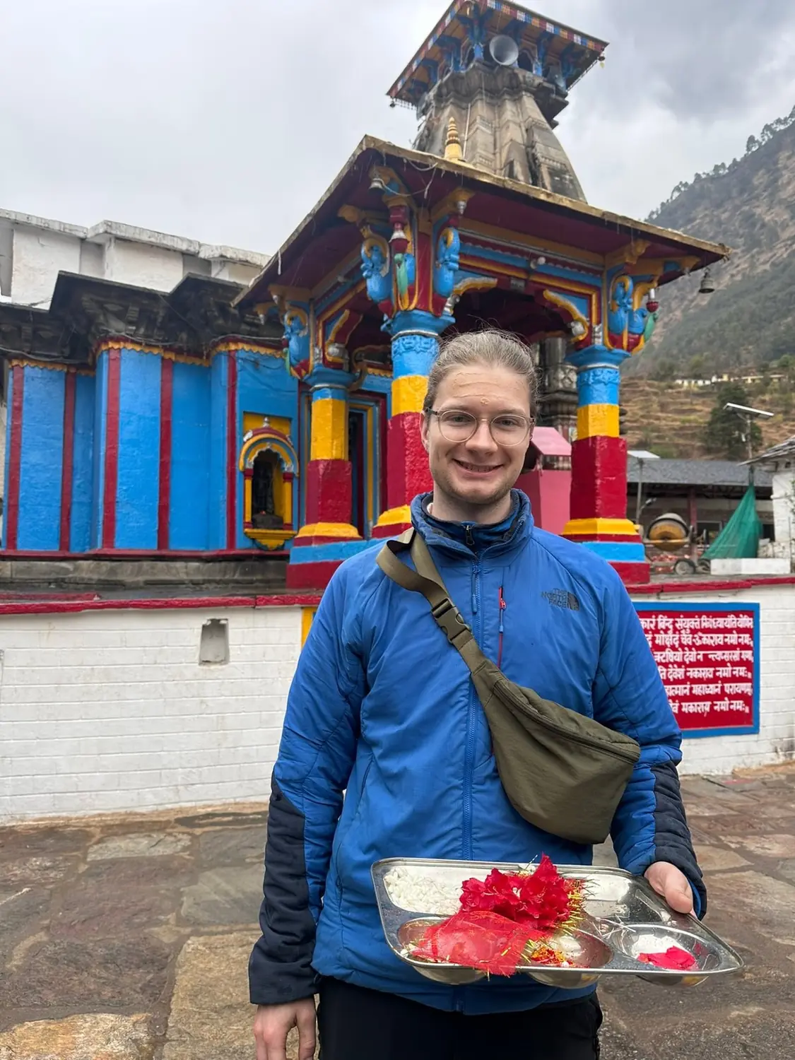 a guest with a prayer plate at the brightly painted mountain temple