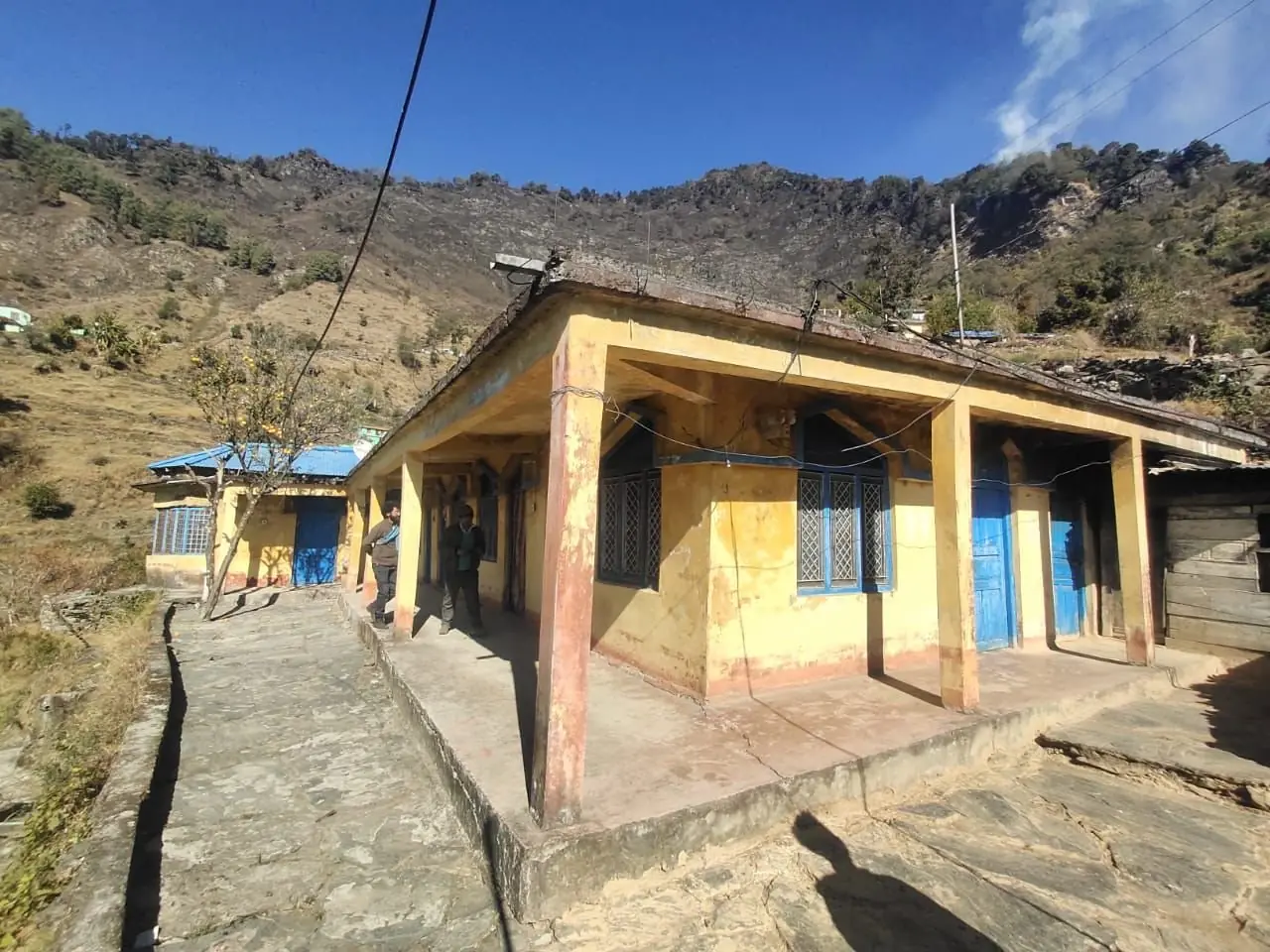 The original yellow mountain building that became The Aipan Retreat, with two people standing on its stone verandah