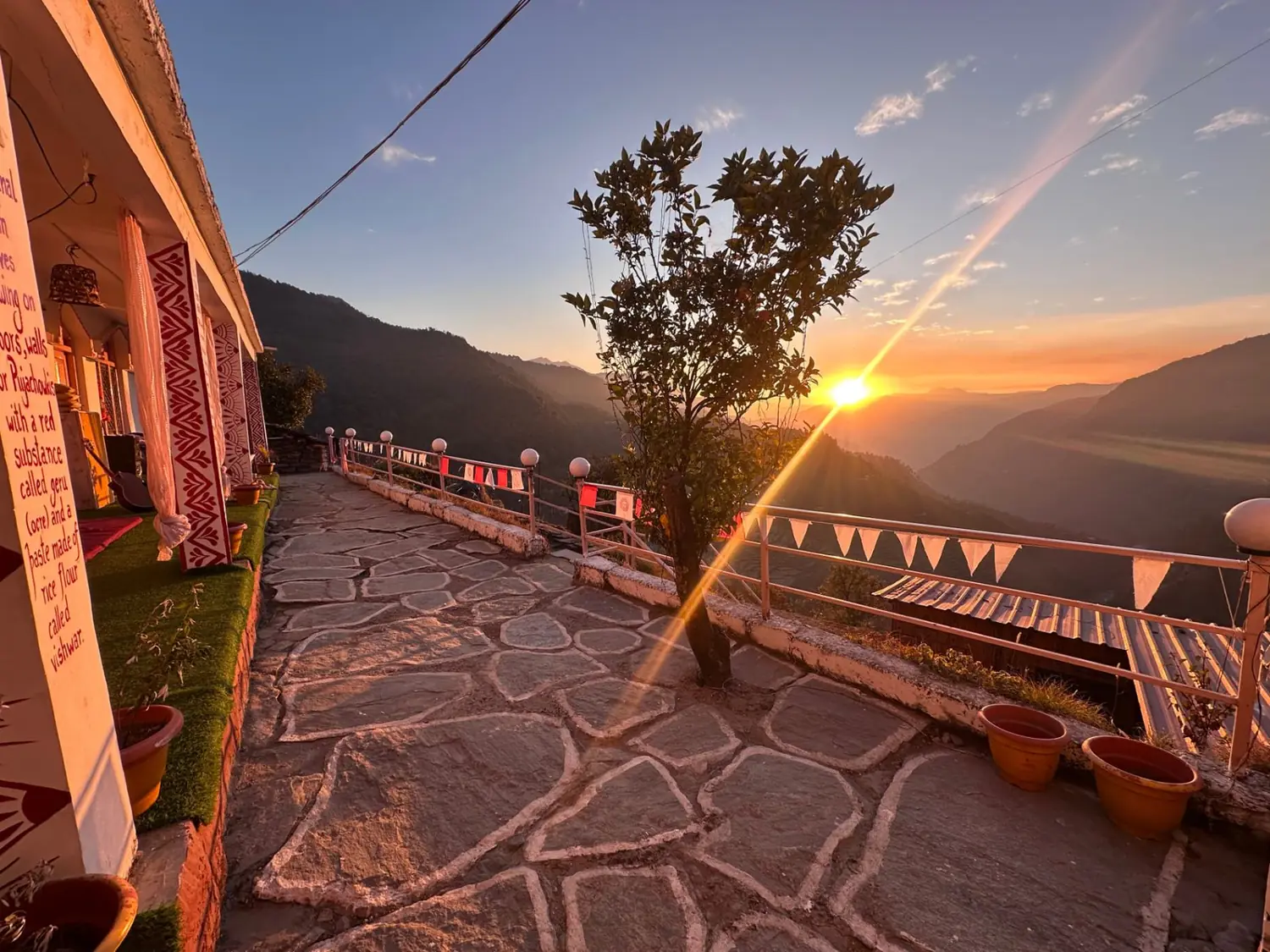 Sunset over the valley from the stone terrace at The Aipan Retreat, with a tree, bunting and the painted verandah