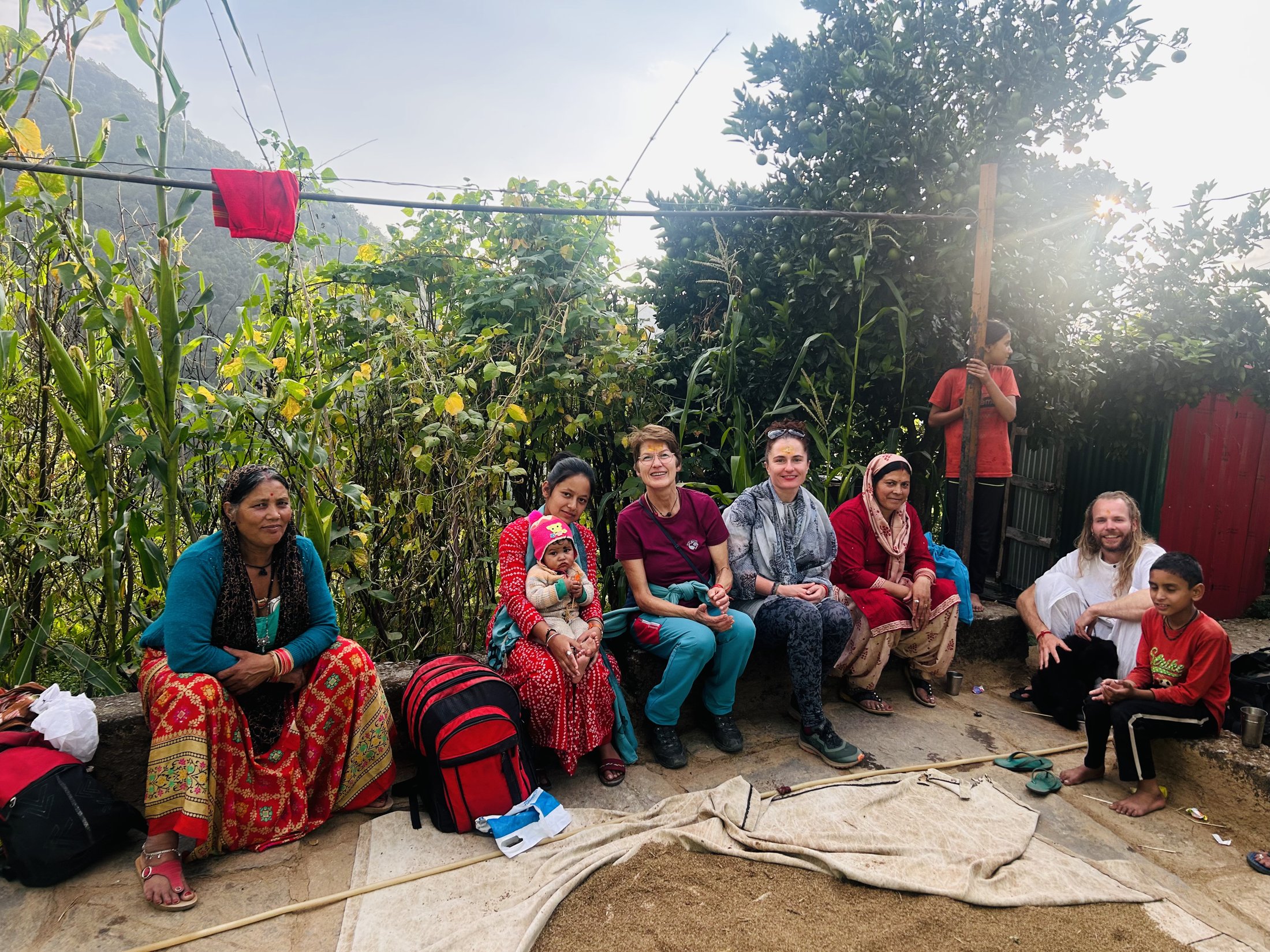 Guests walking through a mountain village with a local farmer, forested Himalayan ridges behind