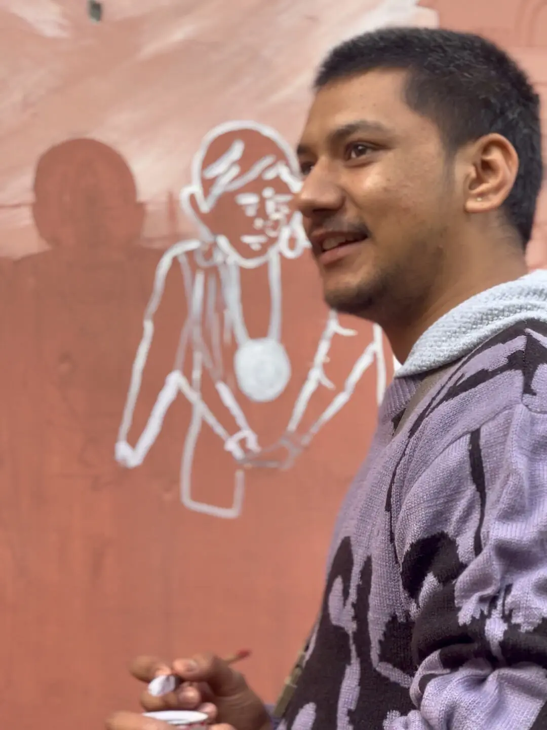A volunteer painting a white Aipan figure onto the red geru wall at the retreat