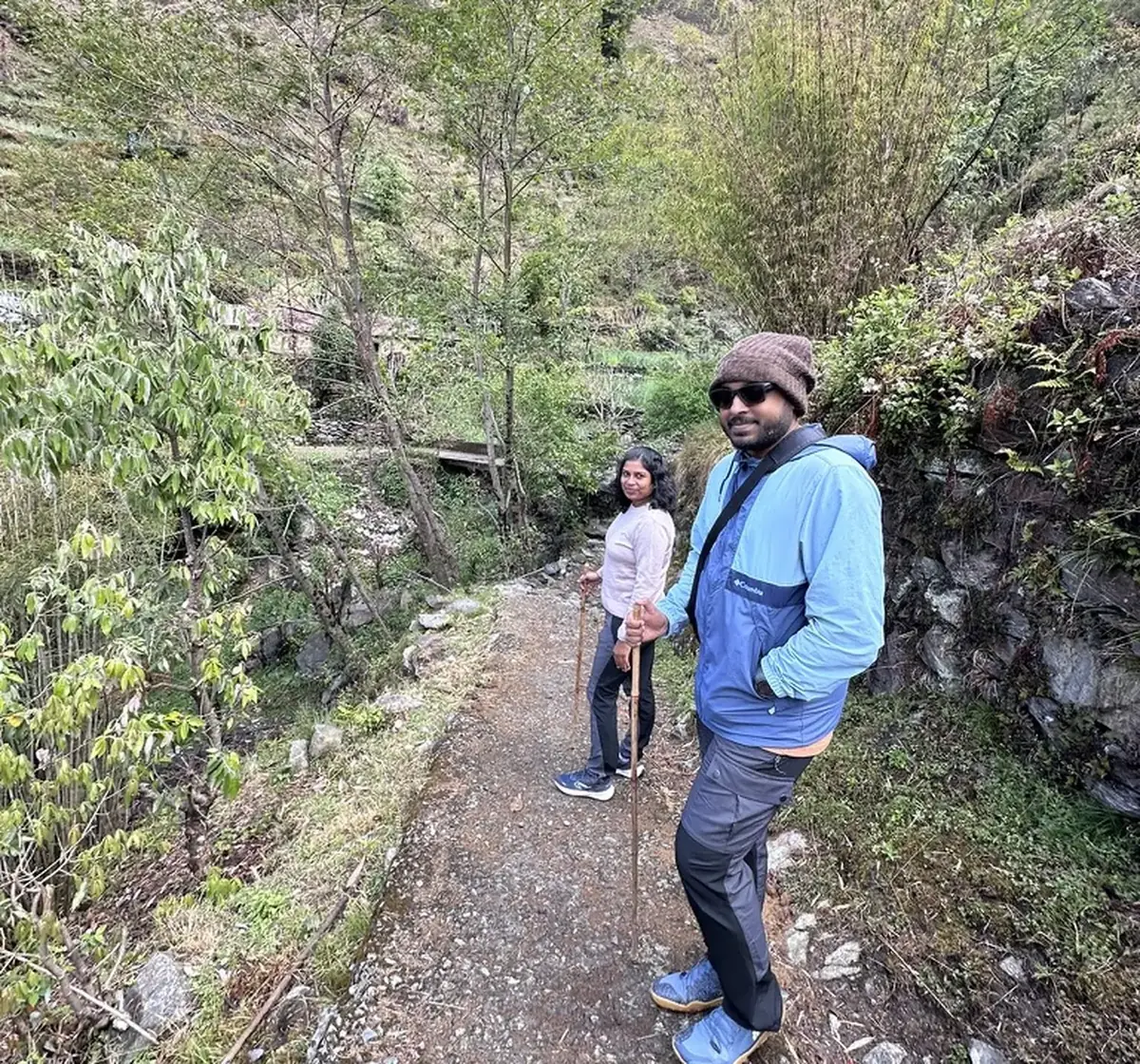Two guests pausing on a forest trail with oak, rhododendron and hillside greenery around them