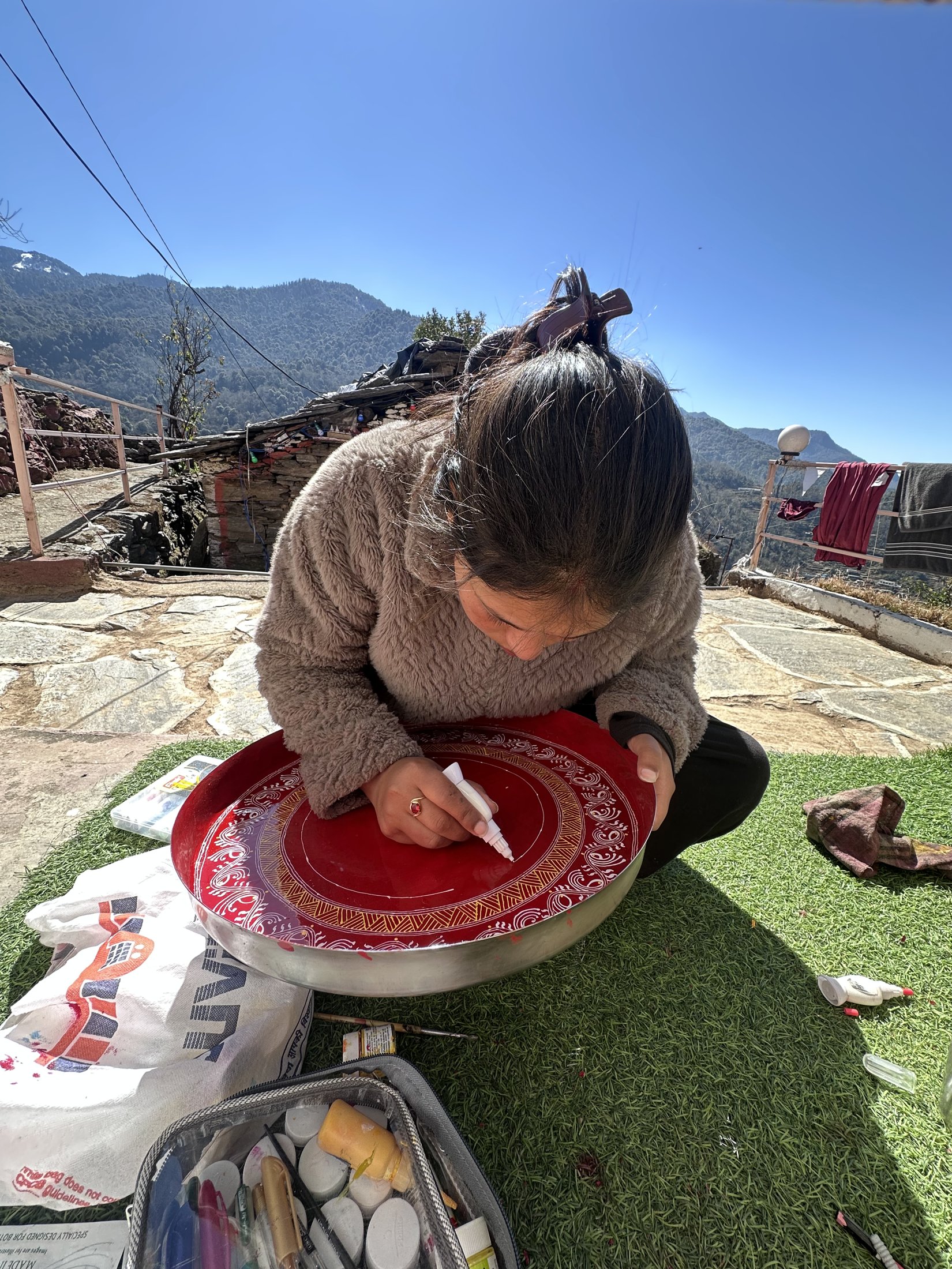 Kajal seated on the floor, hand-painting a traditional Aipan motif in red geru pigment
