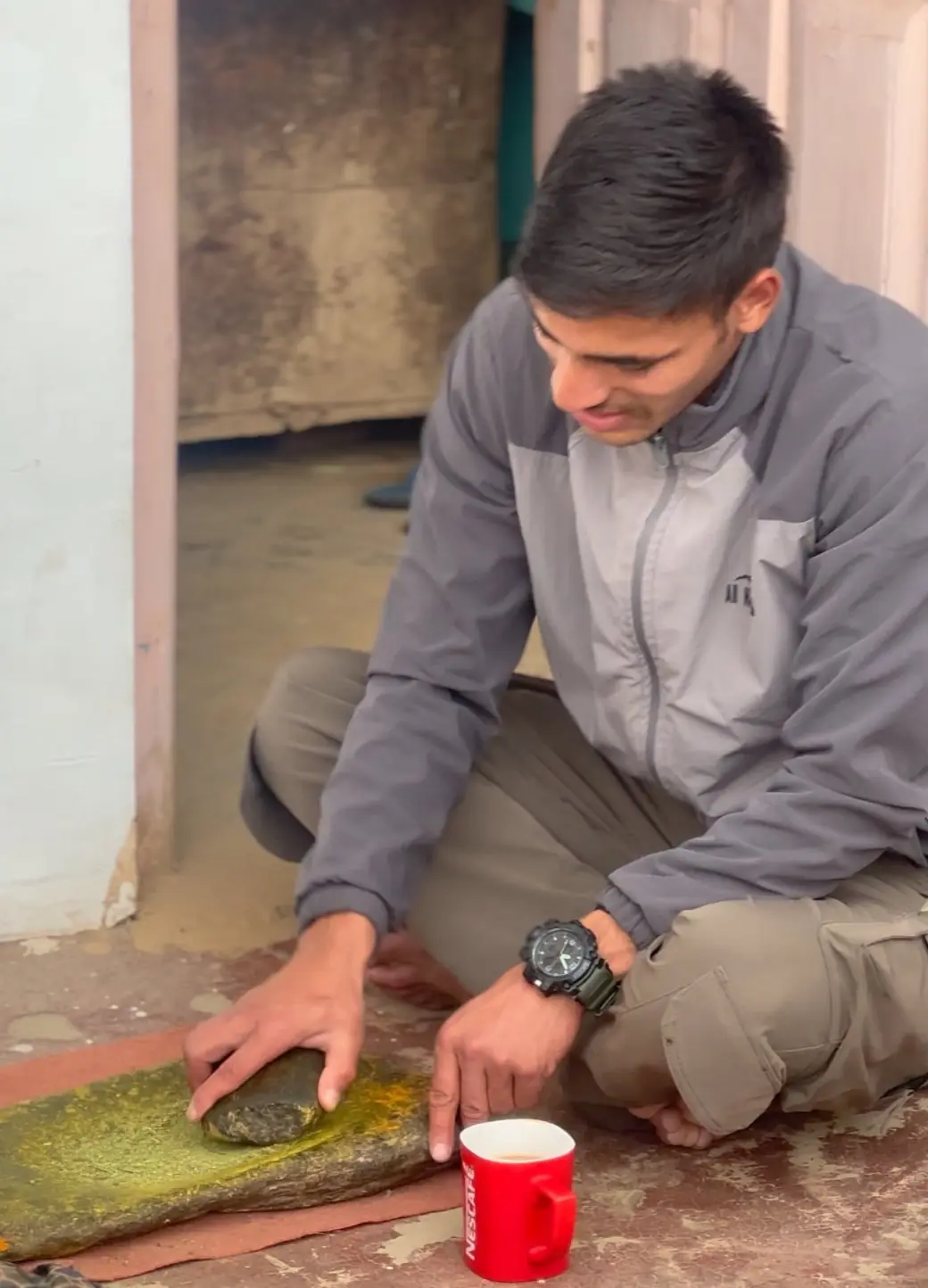 Grinding fresh spices on a traditional stone slab beside a cup of tea