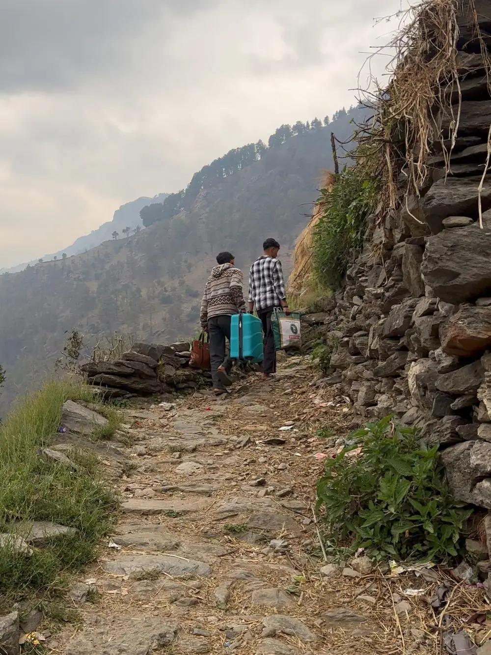 Two men carrying guest luggage up the stone path along the hillside